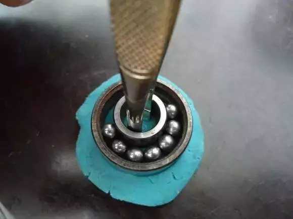 用鑷子或別的相近的物體越過內(nèi)圈，同時(shí)向滾珠的方向用力頂住